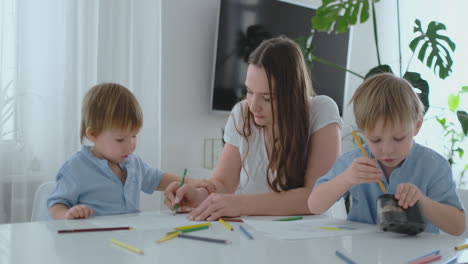 Junge-Mutter-Und-Zwei-Söhne-Im-Alter-Von-2-Bis-4-Jahren-Zeichnen-Bleistifte-Auf-Boomega,-Die-In-Zeitlupe-Am-Wohnzimmertisch-Sitzen